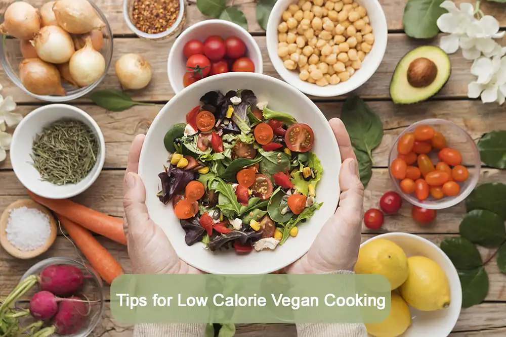 Hands holding a bowl of colorful vegan salad surrounded by fresh ingredients like cherry tomatoes, carrots, chickpeas, herbs, and lemons on a rustic wooden table